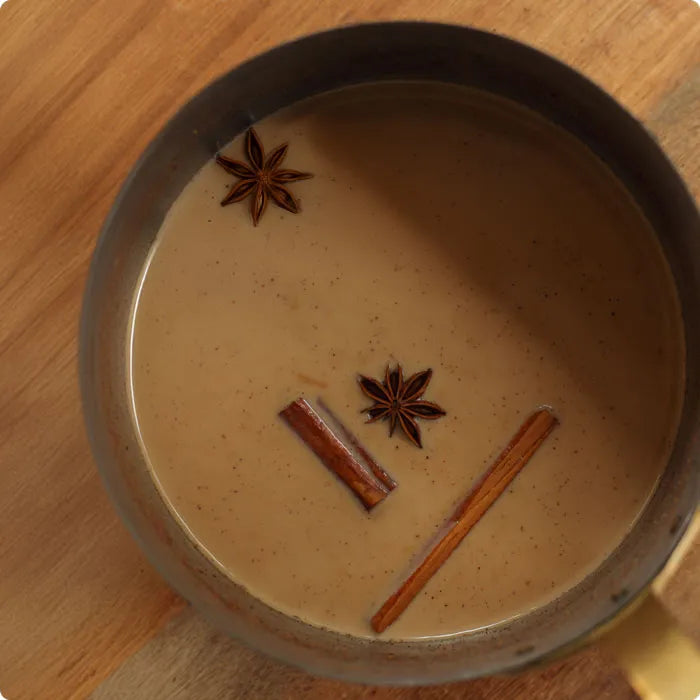 Pouring steamed Chai Masala tea into a ceramic mug using a steam jug.